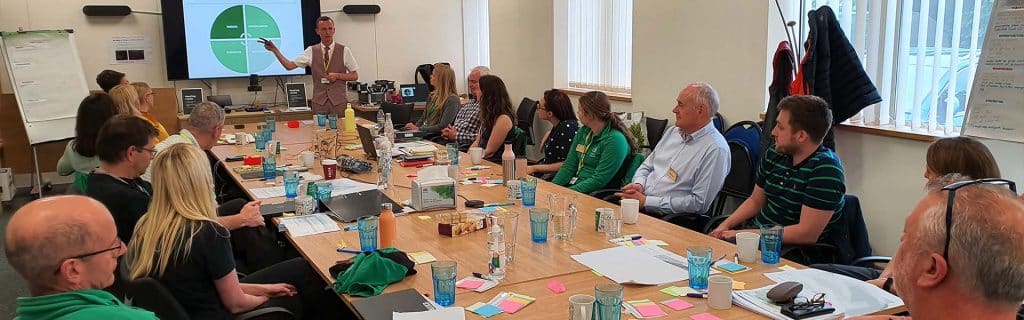 Conference table surrounded by 20 people with one person presenting